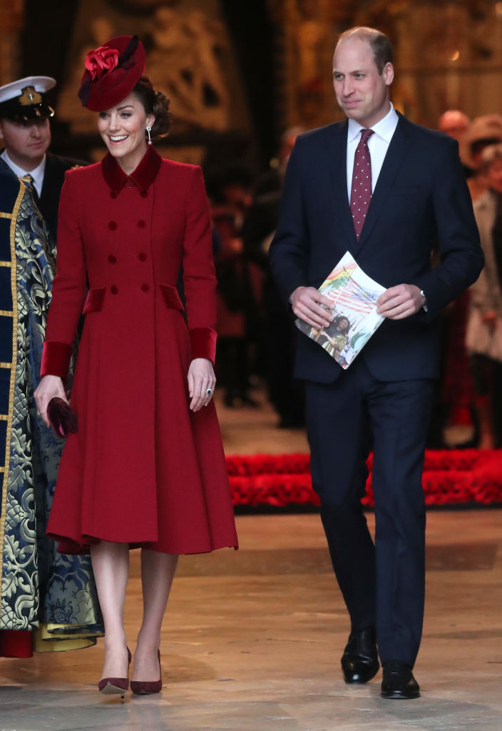 Kate Middleton wearing a red coat dress next to Prince William 