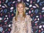 Gwyneth Paltrow smiles in nude dress with floral appliques against blue patterned backdrop