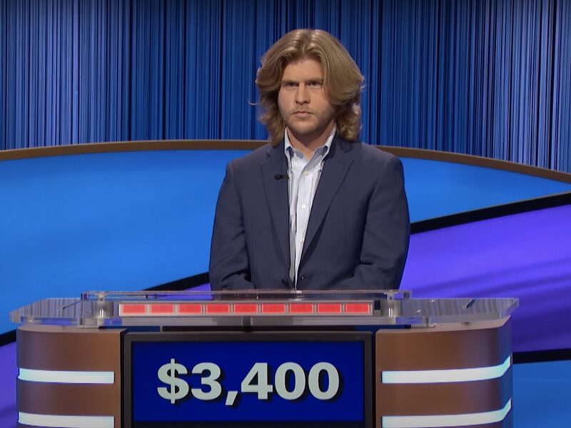 Jimmy Davoren competing on Jeopardy in a blue blazer with just above shoulder length swept blond hair that looks like what the Beegees always wanted