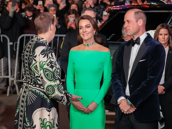 Kate Middleton in a bright green dress with Prince William in a tuxedo talking to a woman on the red carpet