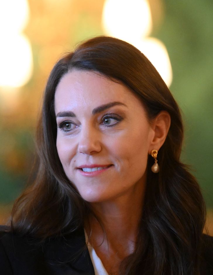 close up of Kate Middleton smiling and looking to her right with a pearl earring on her visible left ear