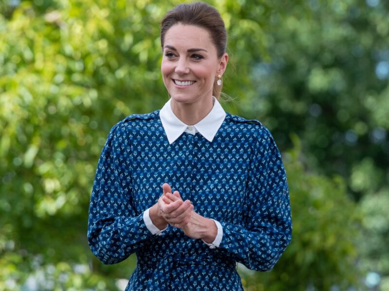 Kate Middleton smiling with hands clasped outdoors in blue dress with white collar