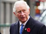 King Charles looks off-camera in black suit and blue polka-dotted tie