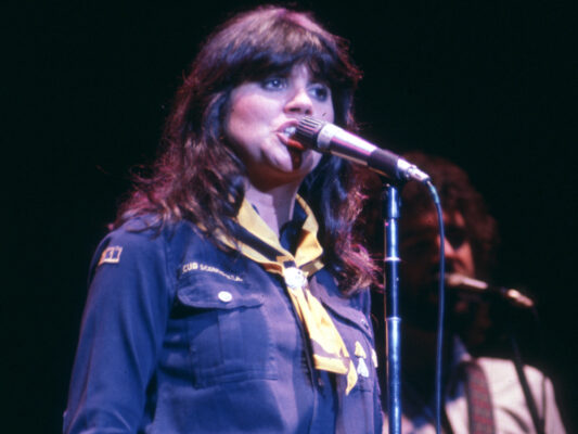 1970s photo of Linda Ronstadt singing into a microphone on a darkened stage