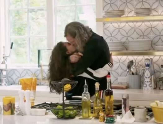 screenshot from Marrying Millions of Bill Hutchinson kissing Brianna Ramirez in a kitchen