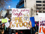 photo of a woman holding up a sign that says "For every single #Me Too Time's Up"