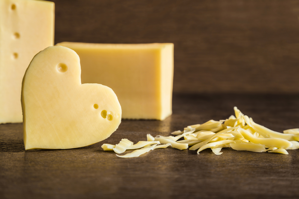 Heart shaped piece of cheese with cheese shavings and blocks in the background. 
