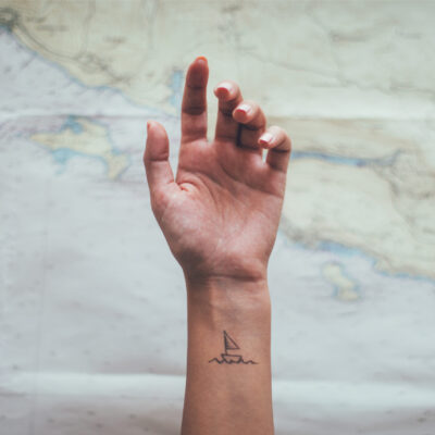 A small simple sailboat tattoo on a woman's wrist