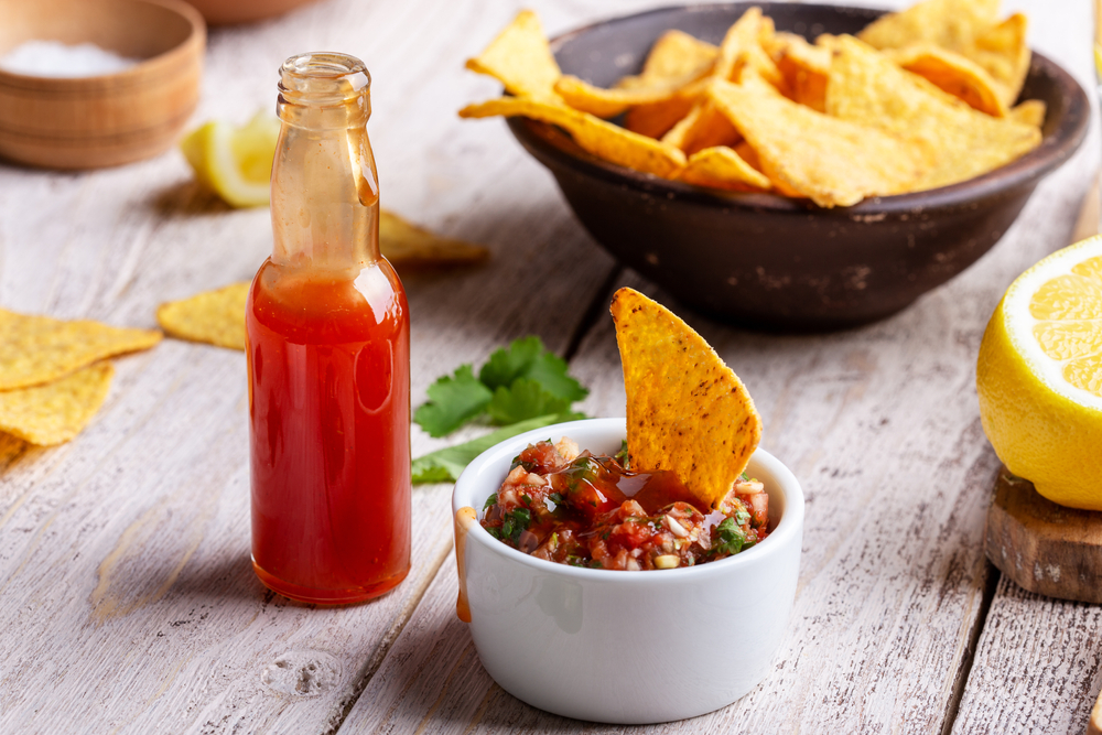 Open jar of hot sauce on table with chips and salsa.