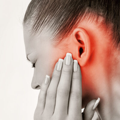 Profile of a woman with her hand near her ear, the ear and surrounding area colored red to signify pain.