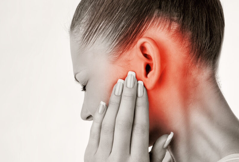 Profile of a woman with her hand near her ear, the ear and surrounding area colored red to signify pain.
