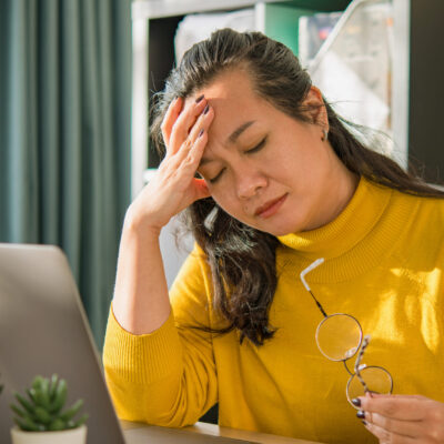 Woman looking stressed with sitting at a desk with an open laptop.