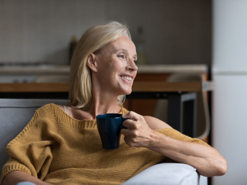 a middle aged woman smiles holding a mug looking into the distance