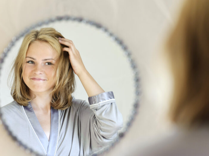 Woman touching her hair in the mirror.