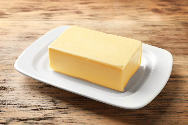 Stick of butter on a white dish sitting on the counter.