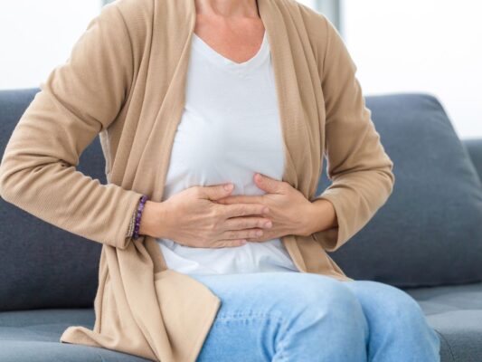 Midlife woman sitting on couch holding her stomach