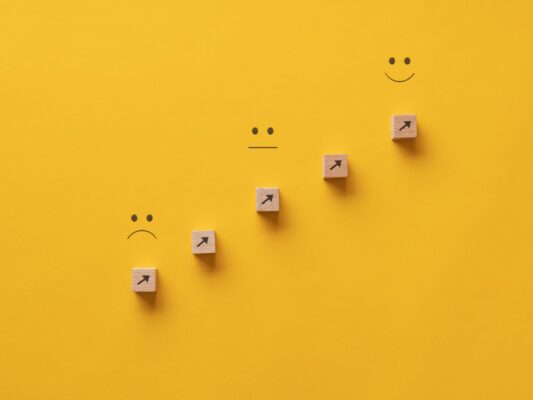 Diagonal upward scale of unhappy to happy faces on bright yellow background