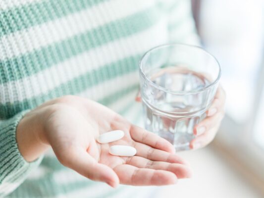 Woman holding a glass of water and a handful of supplements