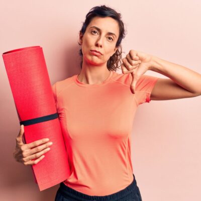 Woman holding a yoga mat with an unhappy expression and thumb down