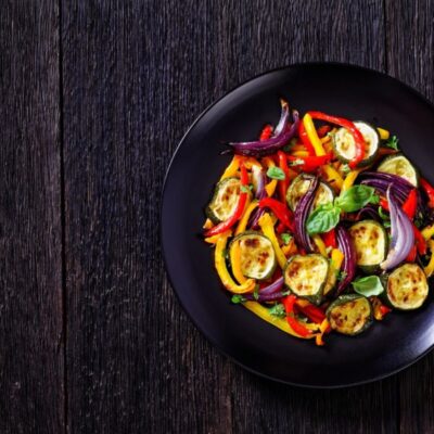 Roasted vegetables sitting on a black plate and dark wood background