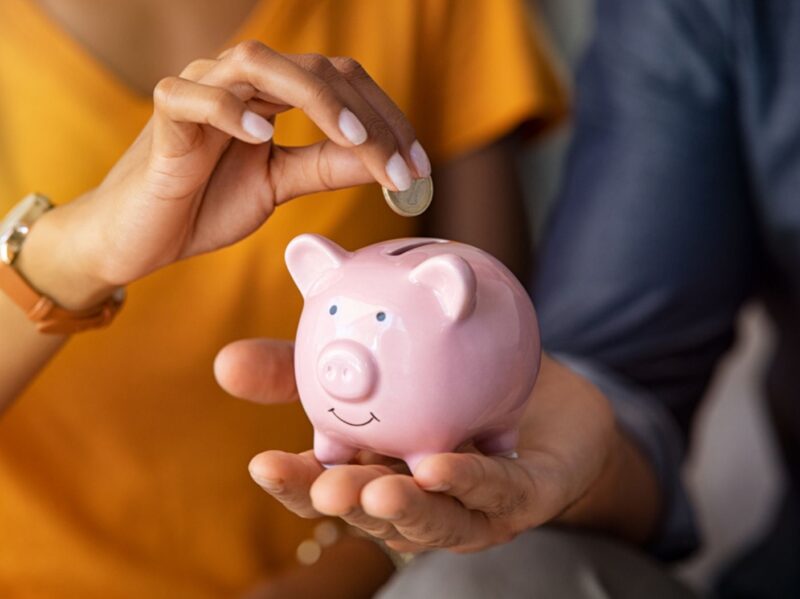 Couple with piggy bank, one partner puts in coin as the other holds it