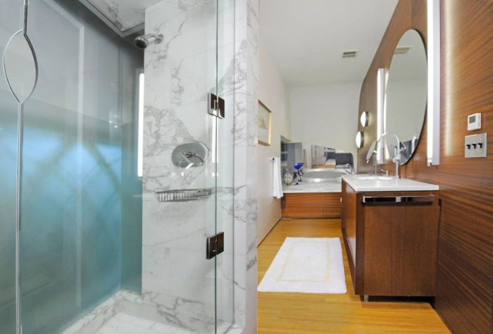 The bathroom features a marble shower and accents of wood on one wall