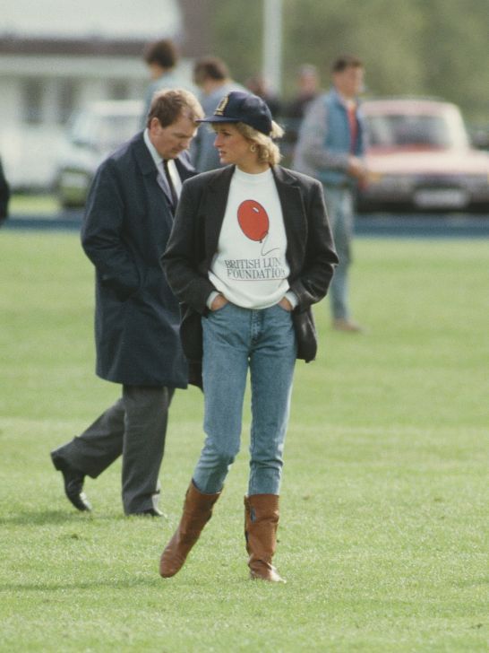 Princess Diana in blazer, sweatshirt, jeans, boots, and cap on lawn