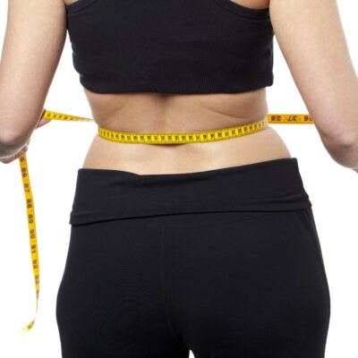 A woman in black workout clothing measures her waist with a tape measure