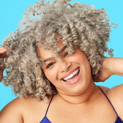 A gray curly haired latina model smiling