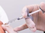 Gloved doctor hand injecting a vial of dermal filler