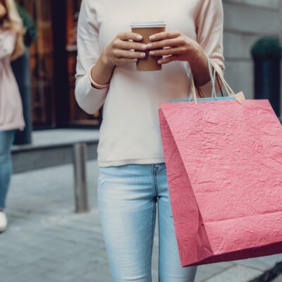 Women holding shopping bags and a cup of coffee with another woman on the phone in the background