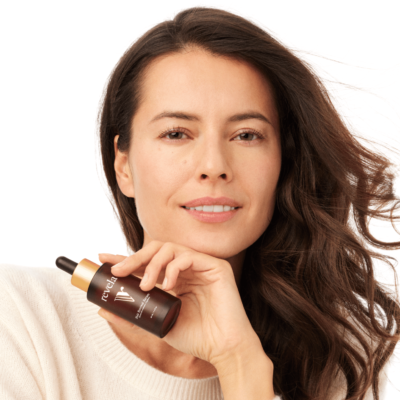 A woman with healthy hair holding a bottle of Revela hair serum