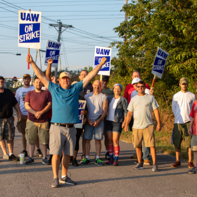 A group of workers on strike walk down a street while holding signs
